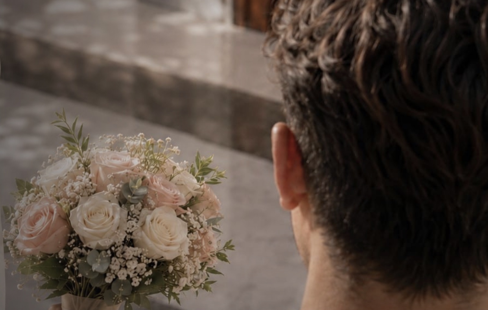 A couple at a wedding, the groom holding a bouquet of pale roses